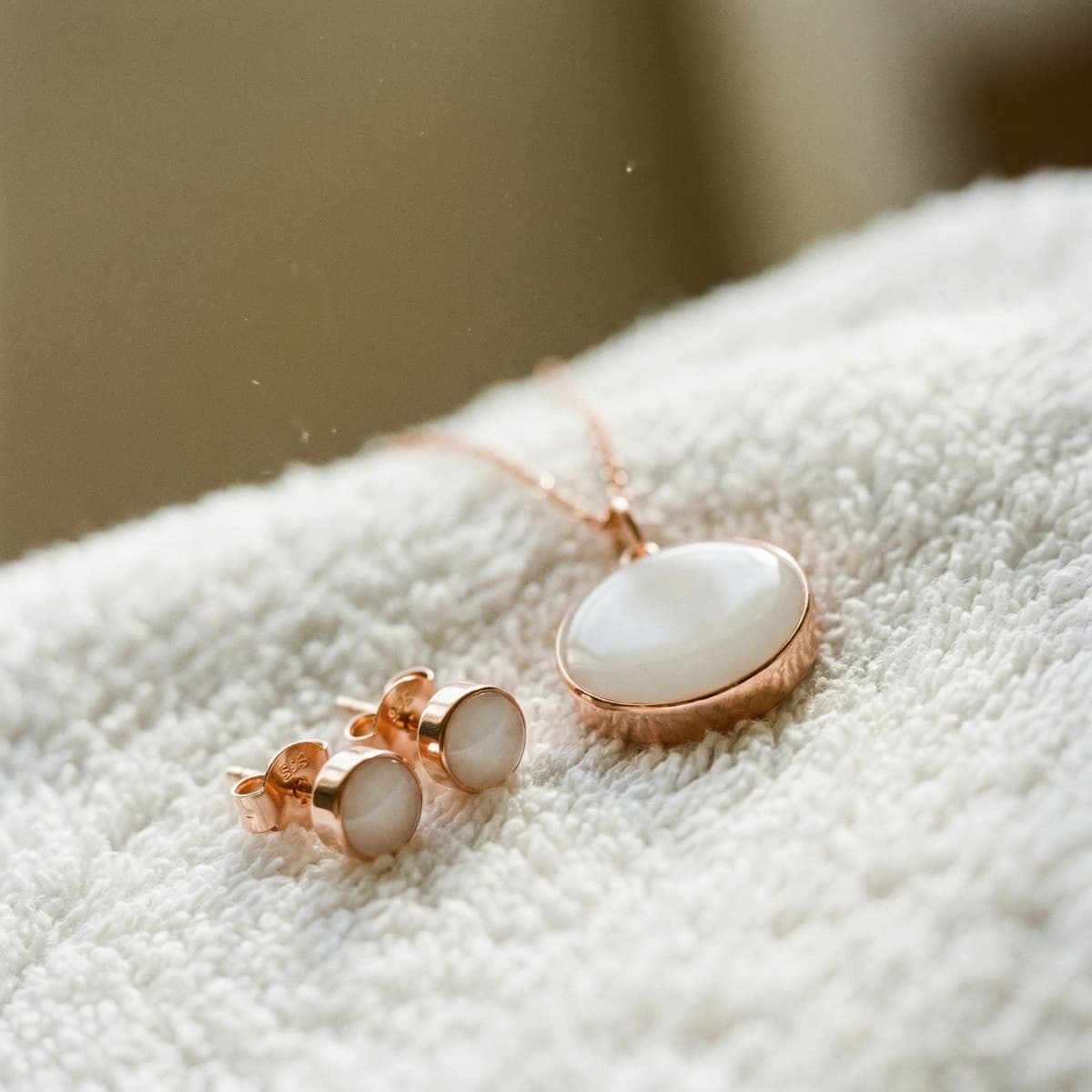 Rose gold breastmilk jewelry set featuring a pendant necklace and matching stud earrings on a soft white towel, celebrating a 1 year breastfeeding award milestone keepsake.