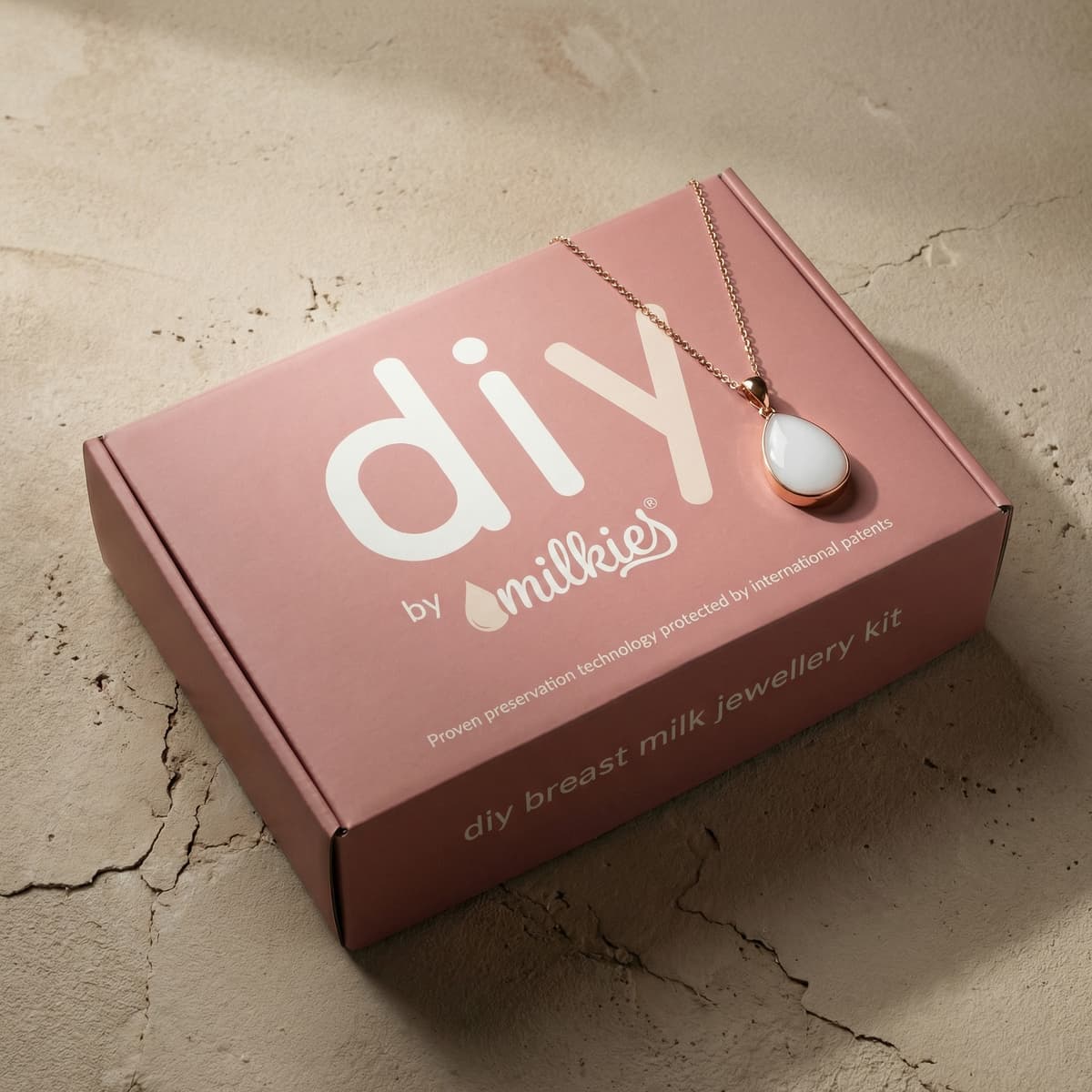 Pink DIY by MILKIES breast milk jewellery kit box showing a rose-gold necklace with white teardrop pendant, an at-home breastfeeding gift for preserving breastmilk as keepsake jewelry.