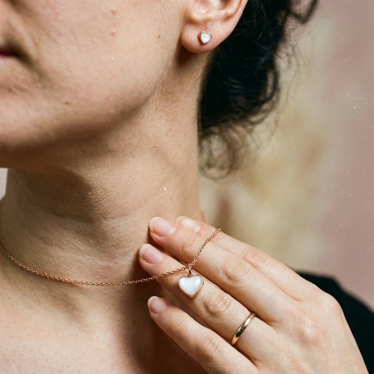 Close-up of a woman wearing a white heart pendant necklace and matching heart stud earrings, a meaningful breastfeeding journey gift keepsake in gold-toned jewelry.