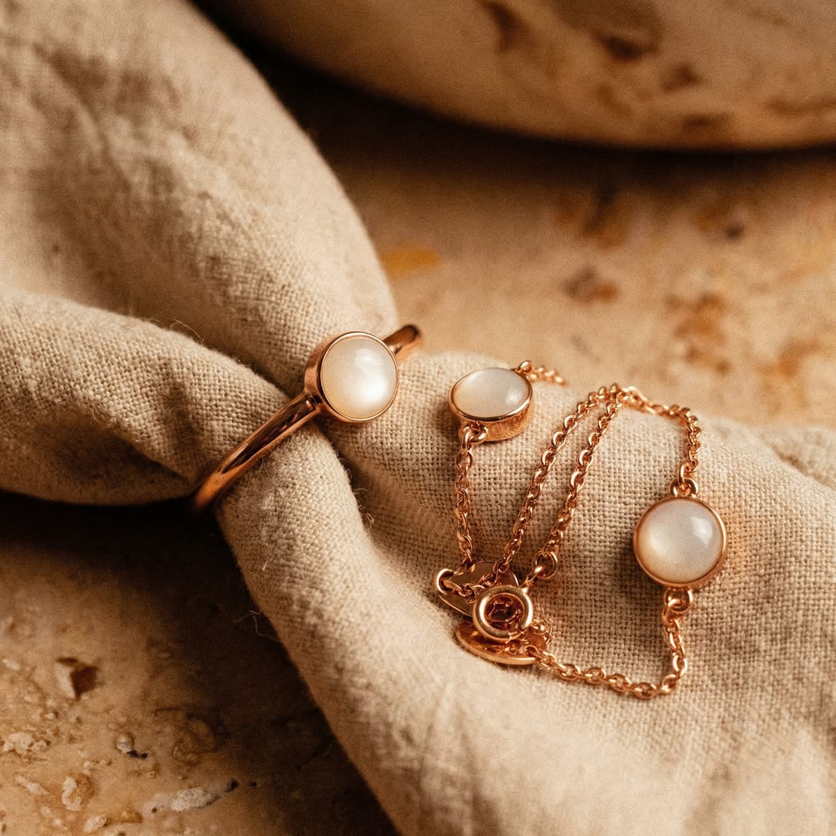 Close-up flat lay of a rose gold breastmilk bracelet with milky white resin stones and a matching ring on soft beige fabric