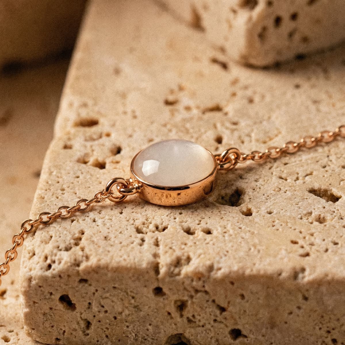 Rose gold chain bracelet featuring an oval milky-white resin stone keepsake, designed as a breastmilk bracelet, resting on a textured beige stone surface