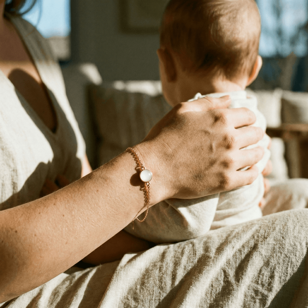 Mother cuddles her baby in warm light while wearing a delicate keepsake bracelet, showing why a breastmilk bracelet diy kit is a meaningful, private way to create memory jewelry at home.