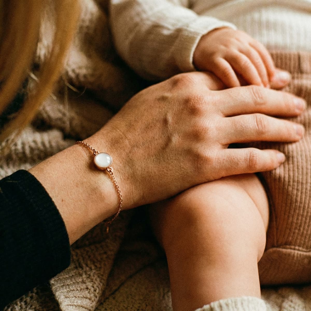 Mother holding her baby while wearing a delicate gold keepsake bracelet with a milky white resin stone from a breastmilk bracelet kit
