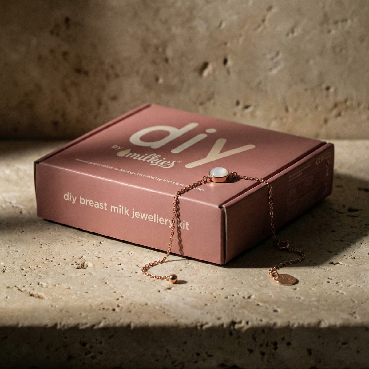 Rose-gold bracelet with a white resin stone displayed over a pink DIY by MILKIES box, showcasing an at-home breastmilk bracelet making kit for creating breast milk jewellery.