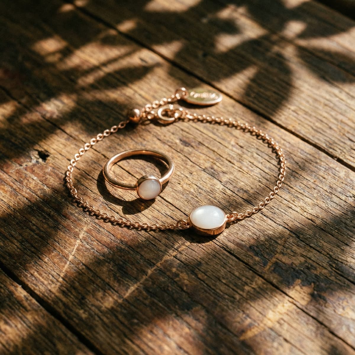 Gold chain bracelet with oval milky-white resin charm and matching ring on a rustic wooden surface in warm sunlight, an elegant example of breastmilk bracelets