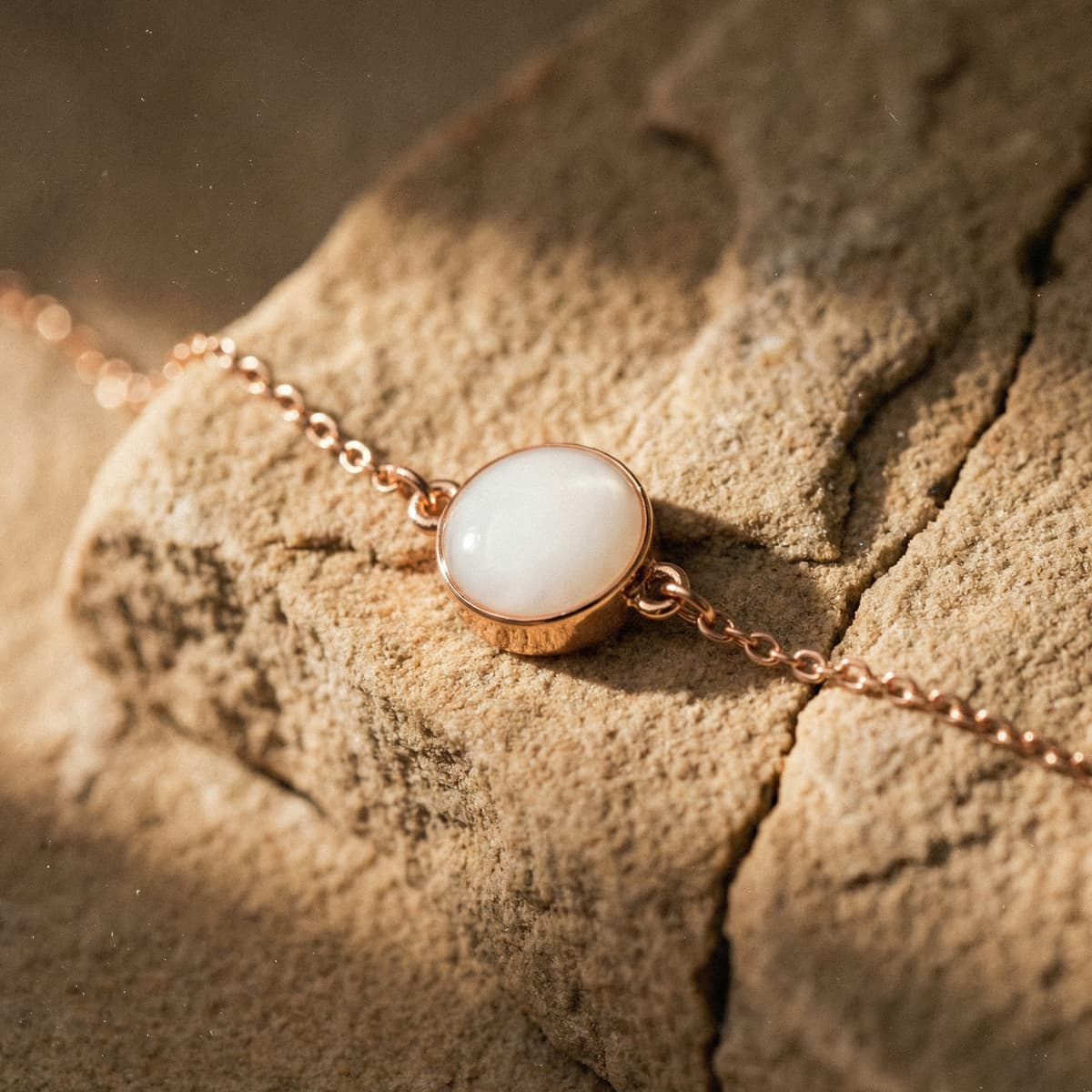 Rose gold chain bracelet featuring a smooth milky-white resin stone, showcasing elegant breastmilk bracelets on a textured sand-colored surface.