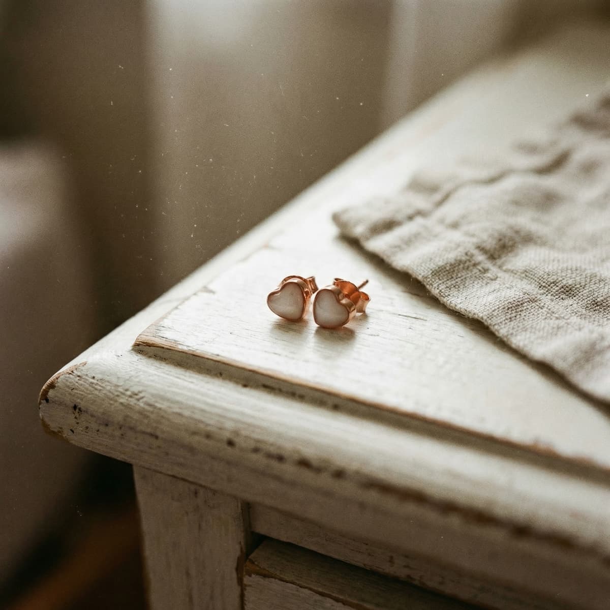 Rose gold heart stud earrings with milky white resin displayed on a rustic wooden table, styled as a breastmilk earring diy kit keepsake next to a soft linen cloth.