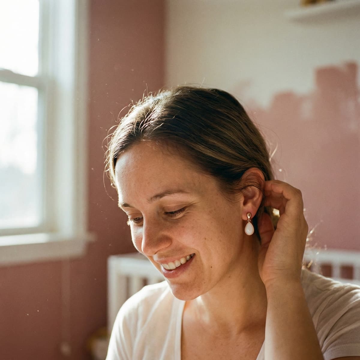 Smiling mom in warm morning light wearing a teardrop keepsake earring, showing why an at-home breastmilk earring making kit is a meaningful DIY way to create a personal memento.