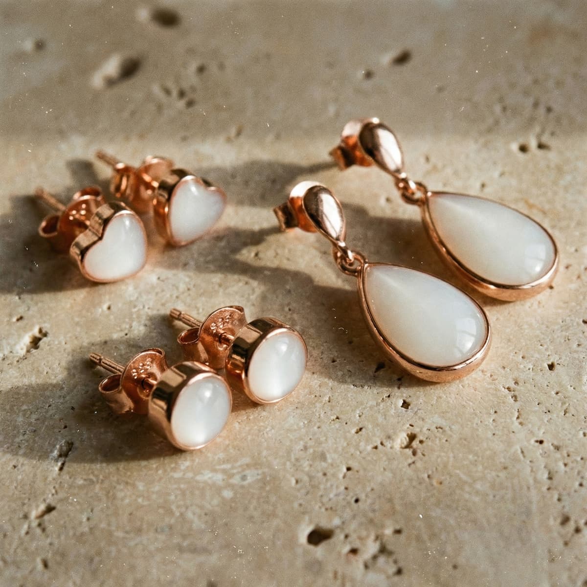 Rose gold jewelry set featuring breastmilk earrings with milky white resin stones, including heart studs, round studs, and teardrop dangle earrings on a neutral textured background.