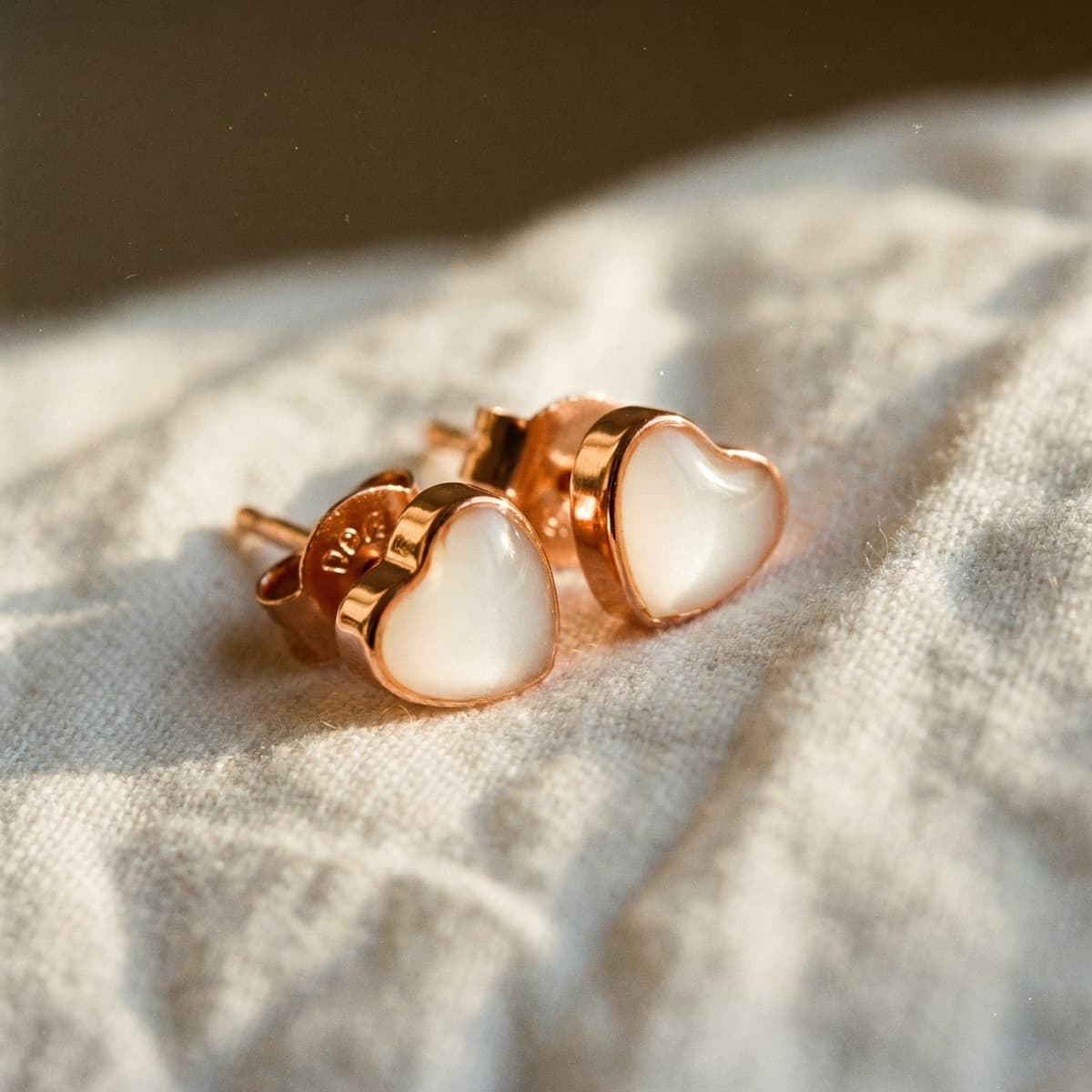 Heart-shaped rose gold breastmilk keepsake stud earrings made using a breastmilk earrings diy kit, displayed on soft beige fabric background.