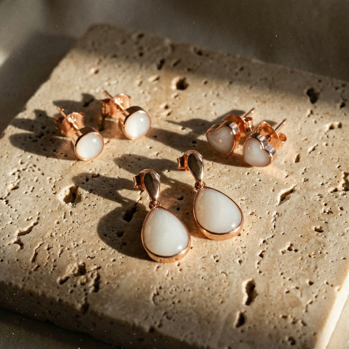 Rose gold and white resin earrings on a textured stone, showcasing teardrop dangles, heart studs, and round studs made with a breastmilk earrings kit