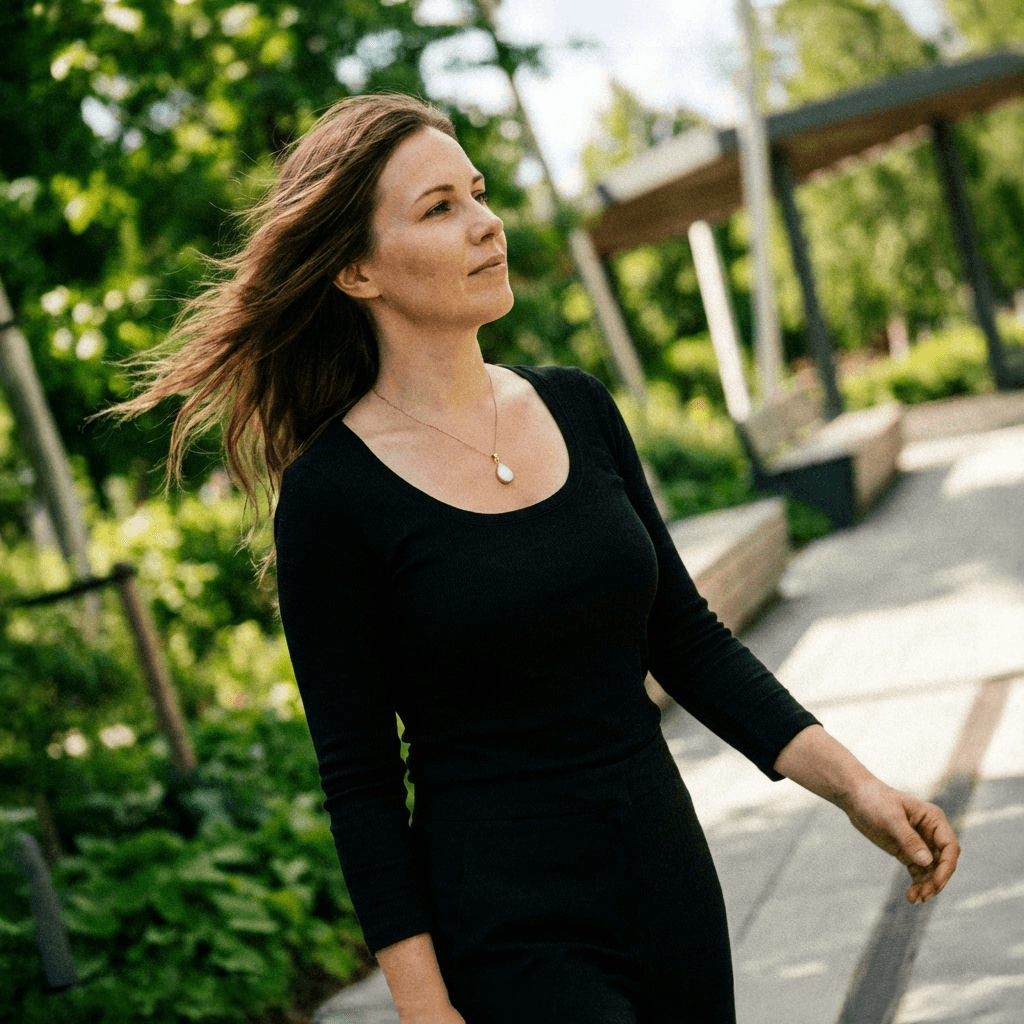 Woman walking outdoors in a black dress wearing a delicate pendant, showcasing personalized breastmilk necklaces as a sentimental keepsake jewelry piece.