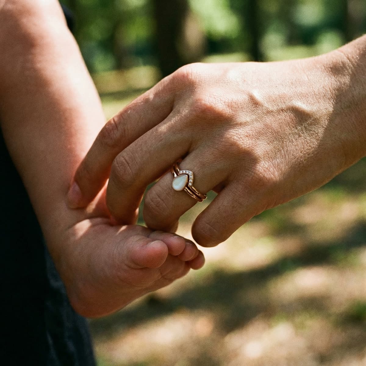 Mother holding a baby’s foot while wearing a gold breastmilk keepsake ring made with a breastmilk ring diy kit, featuring an oval milky stone and tiny diamonds outdoors