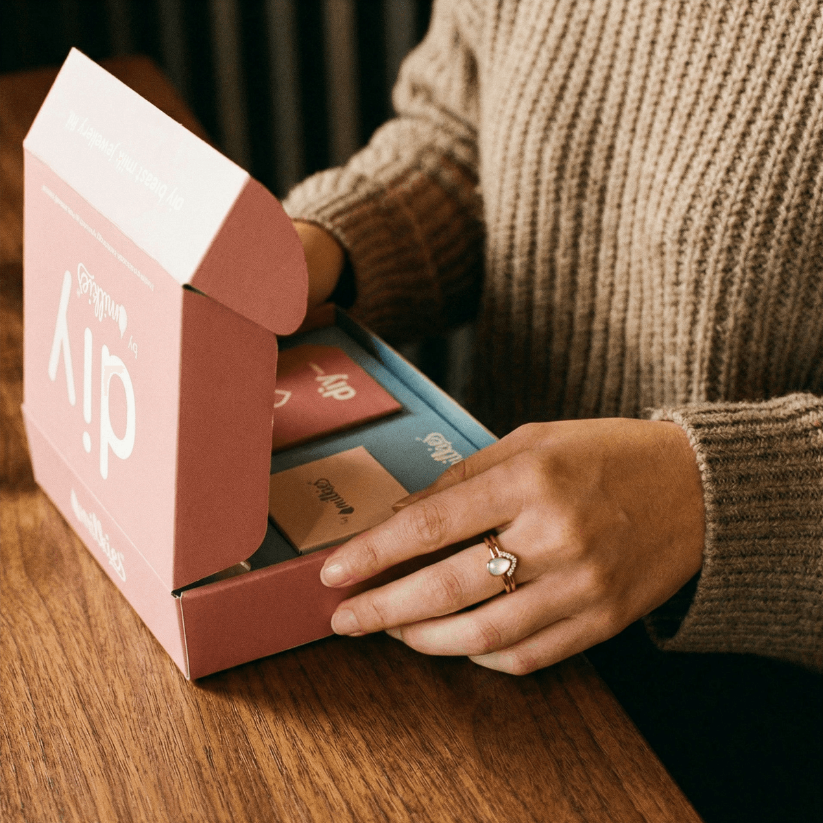 Mother unboxing the DIY by MILKIES kit on a wooden table, showing tools and materials for making breastmilk rings at home as a private, hands-on keepsake option.