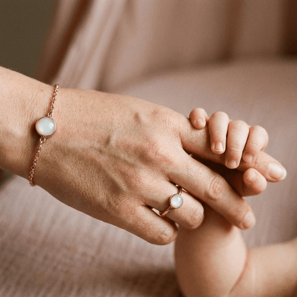 Mother holding a baby’s hand while wearing a delicate gold bracelet with a milky-white resin charm, showcasing a diy breastmilk bracelet keepsake idea.