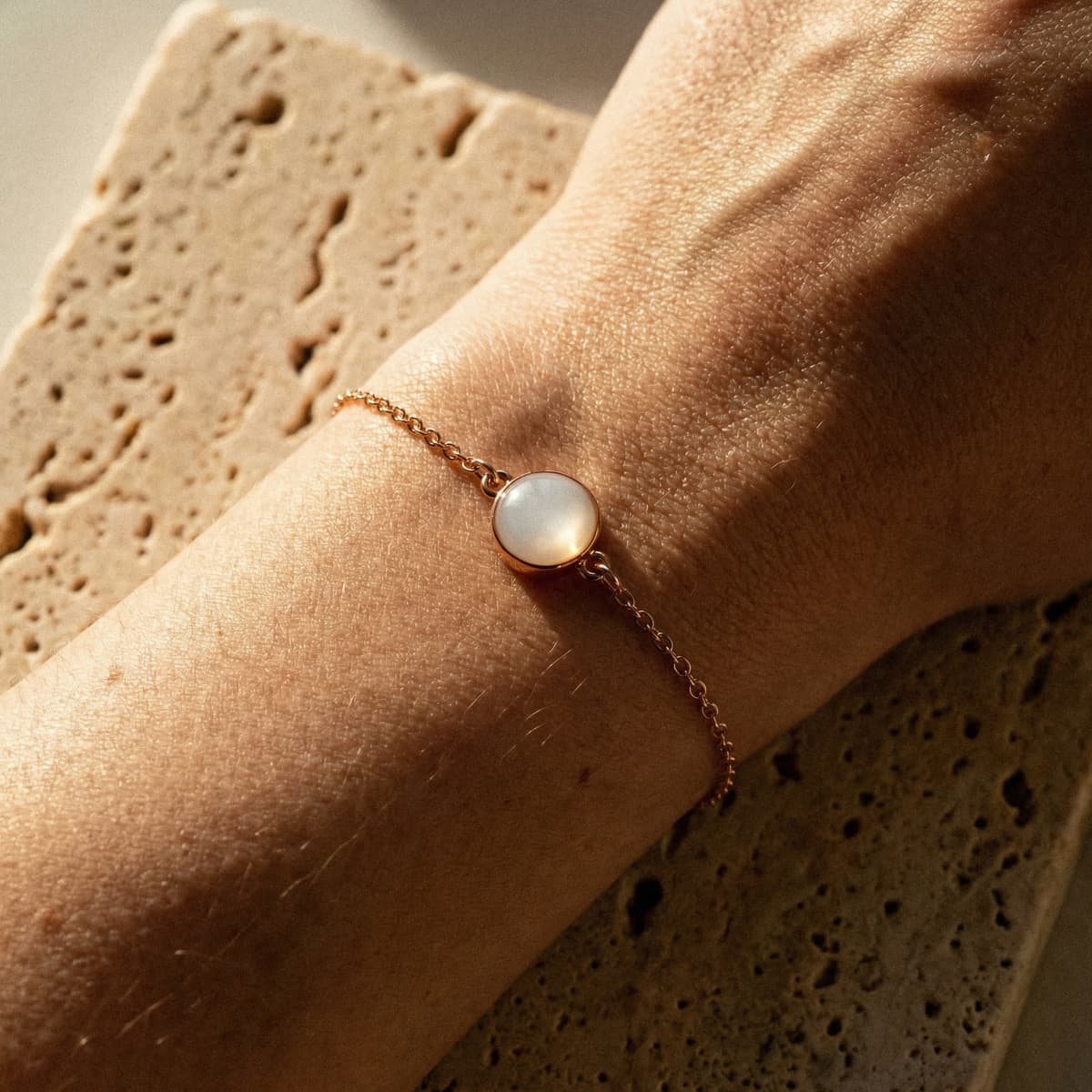 Minimalist gold chain bracelet with a round milky-white resin stone, representing diy breastmilk bracelets as a delicate keepsake worn on a wrist in warm natural light.