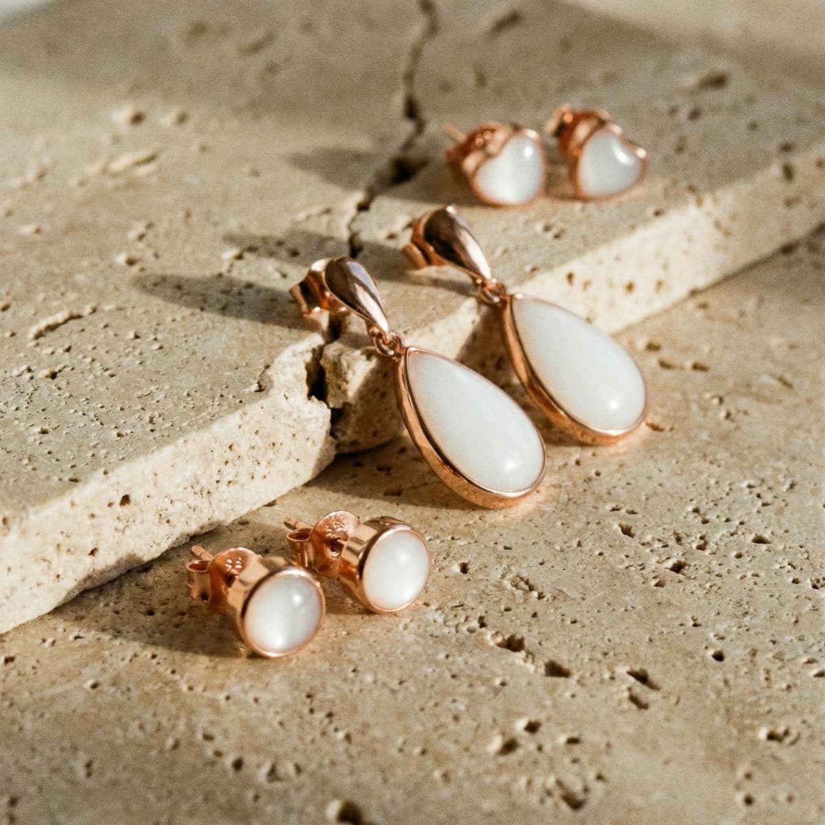 Rose gold drop and stud earrings with milky white resin stones on a textured stone surface, showcased as a diy breastmilk earring keepsake set.