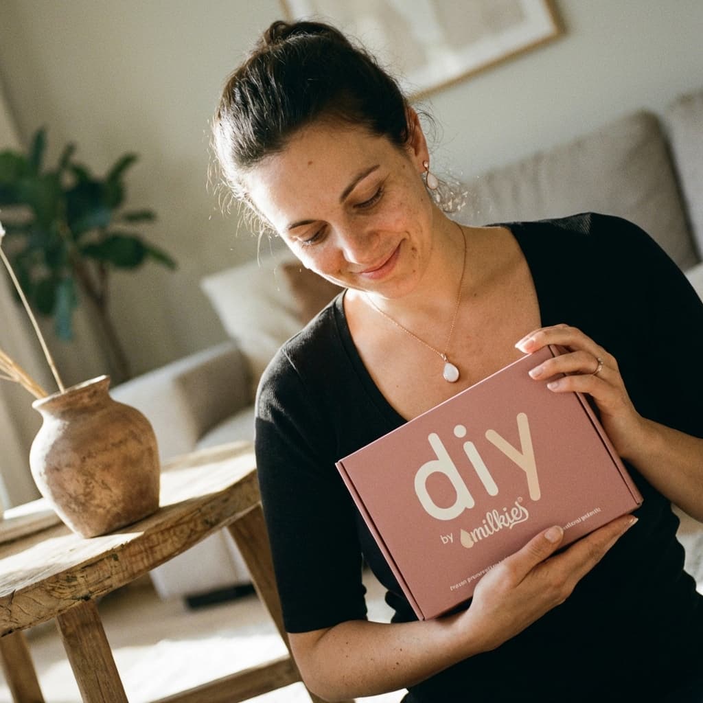Smiling mother at home holding a pink DIY by MILKIES box, showing why a diy breastmilk jewellery kit is a convenient, private way to create a meaningful keepsake yourself.