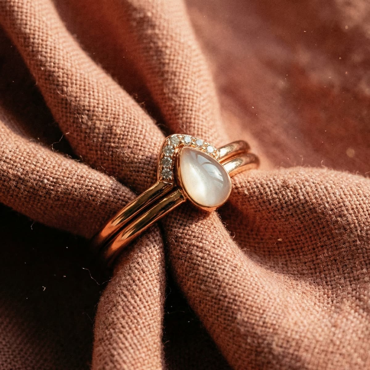 Rose gold keepsake ring made with a diy breastmilk ring kit, featuring a pear-shaped milky resin stone surrounded by a delicate diamond halo on soft textured fabric.