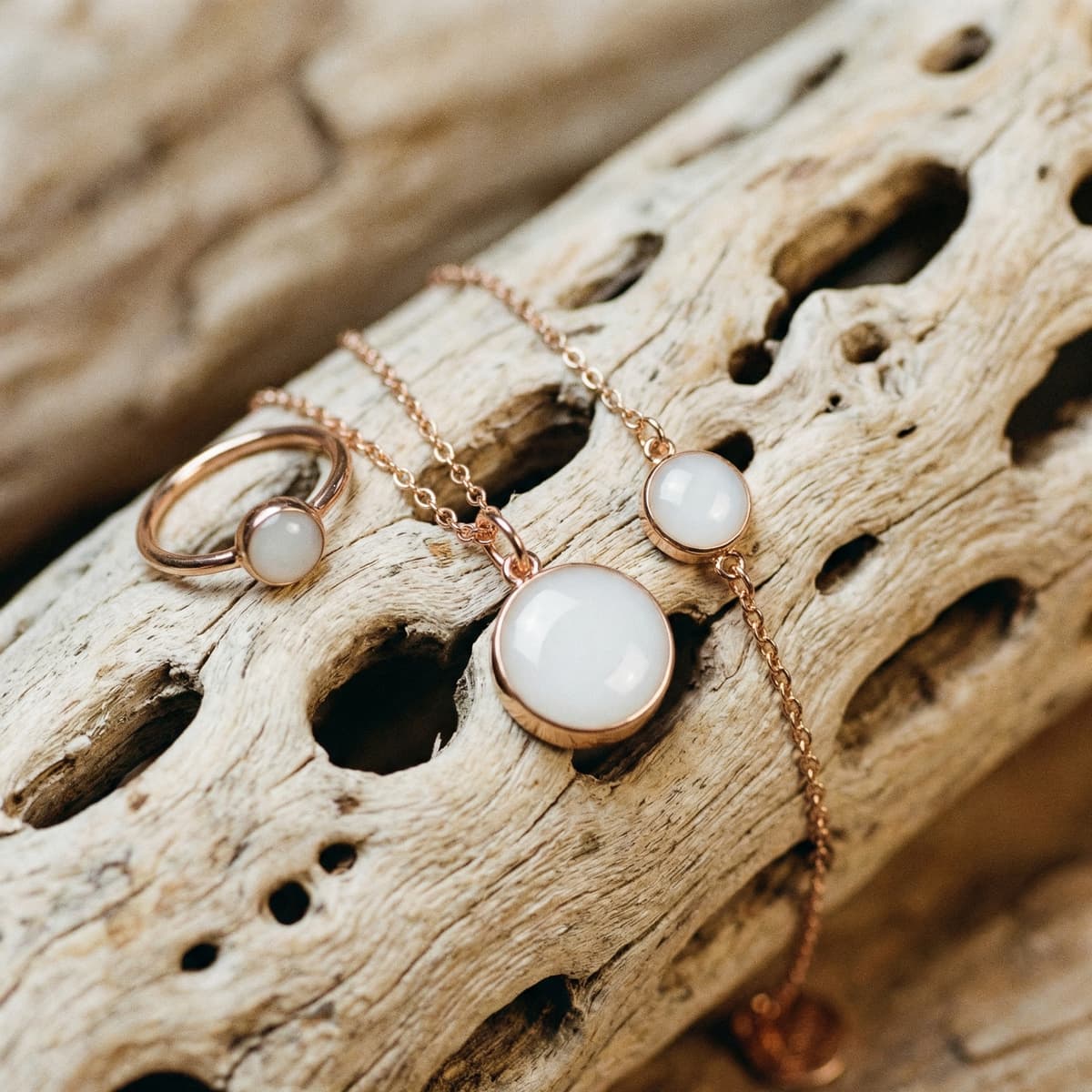 Rose gold breastmilk jewelry set on driftwood with a ring and two pendants featuring milky white resin stones, a keepsake for moms during drying up milk after breastfeeding.