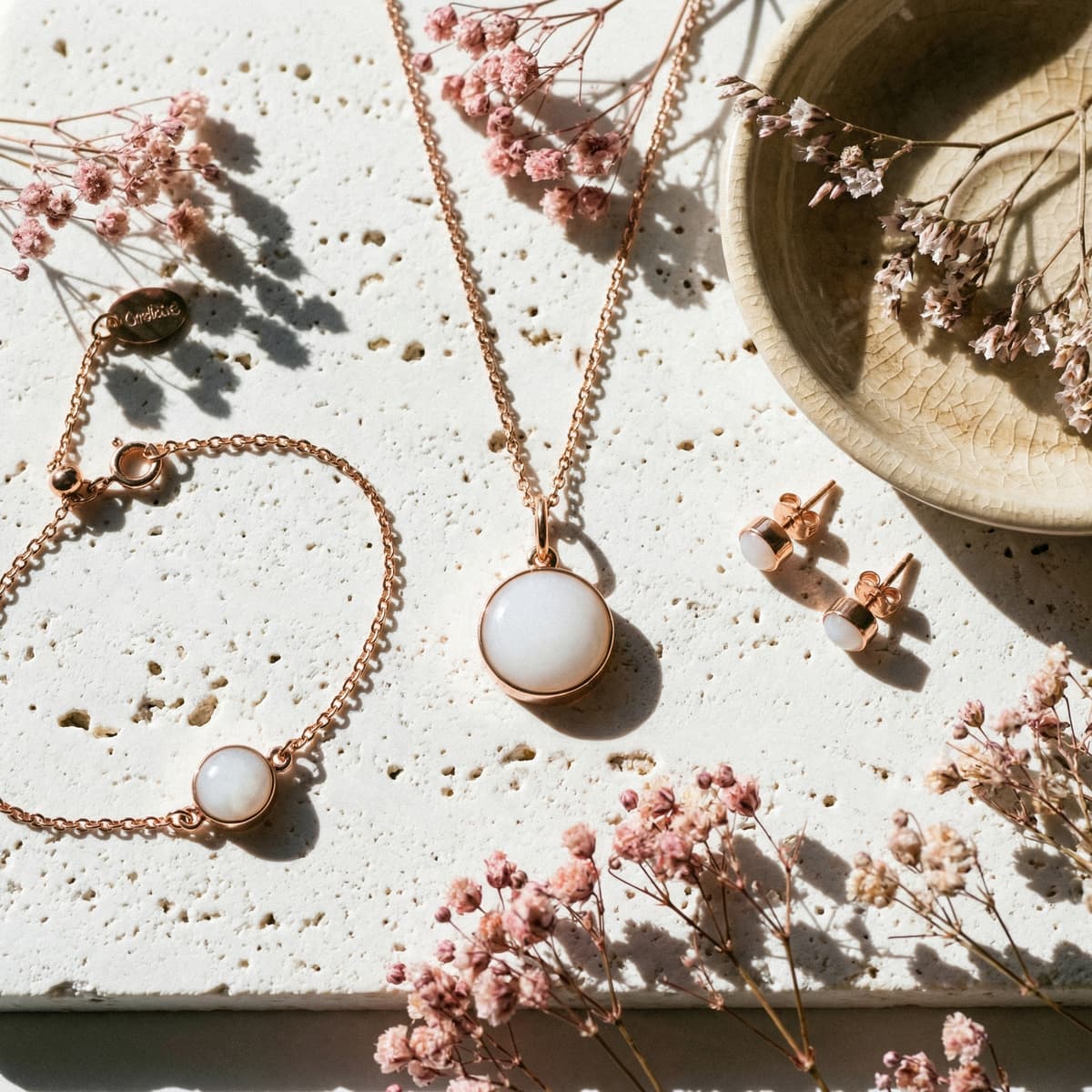 Rose gold breastmilk jewelry set featuring a round milky-white pendant necklace with matching stud earrings and bracelet, styled with dried pink flowers as an elegant end of breastfeeding gift