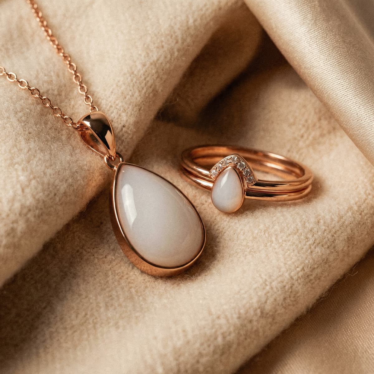 Rose gold teardrop pendant necklace and matching ring with a milky white resin stone, a delicate last feed keepsake jewelry set displayed on soft beige fabric.