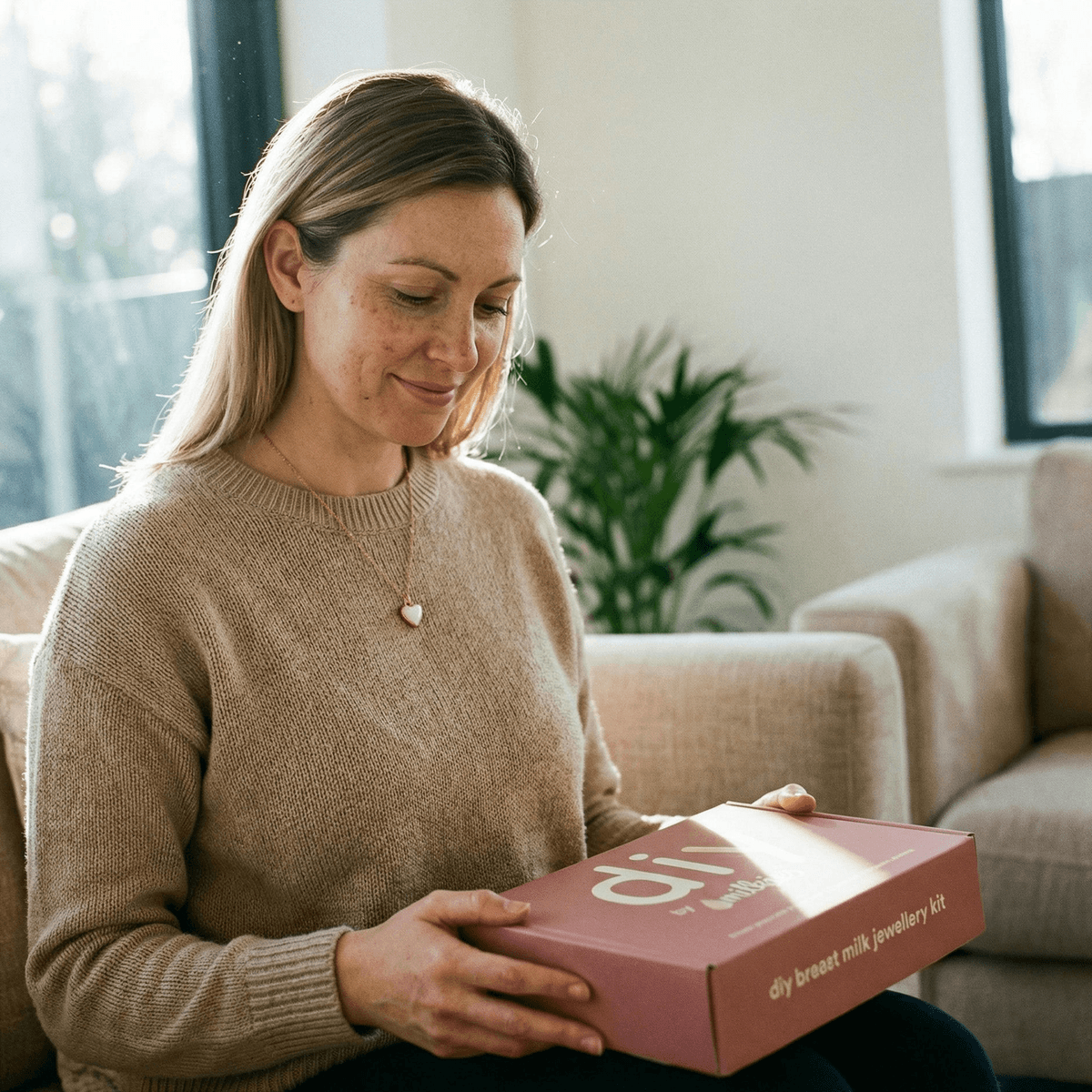 Mother at home holding DIY by MILKIES breast milk jewellery kit box, showing why an at-home process is a good idea for creating a private, hands-on last feed keepsake.