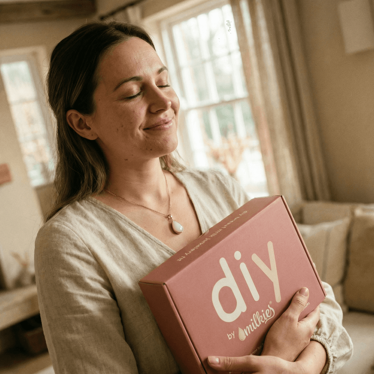 Mother at home holding a pink DIY by MILKIES breastmilk keepsake kit box, reflecting on the last latch and why an at-home hands-on kit is a meaningful choice for preserving memories.