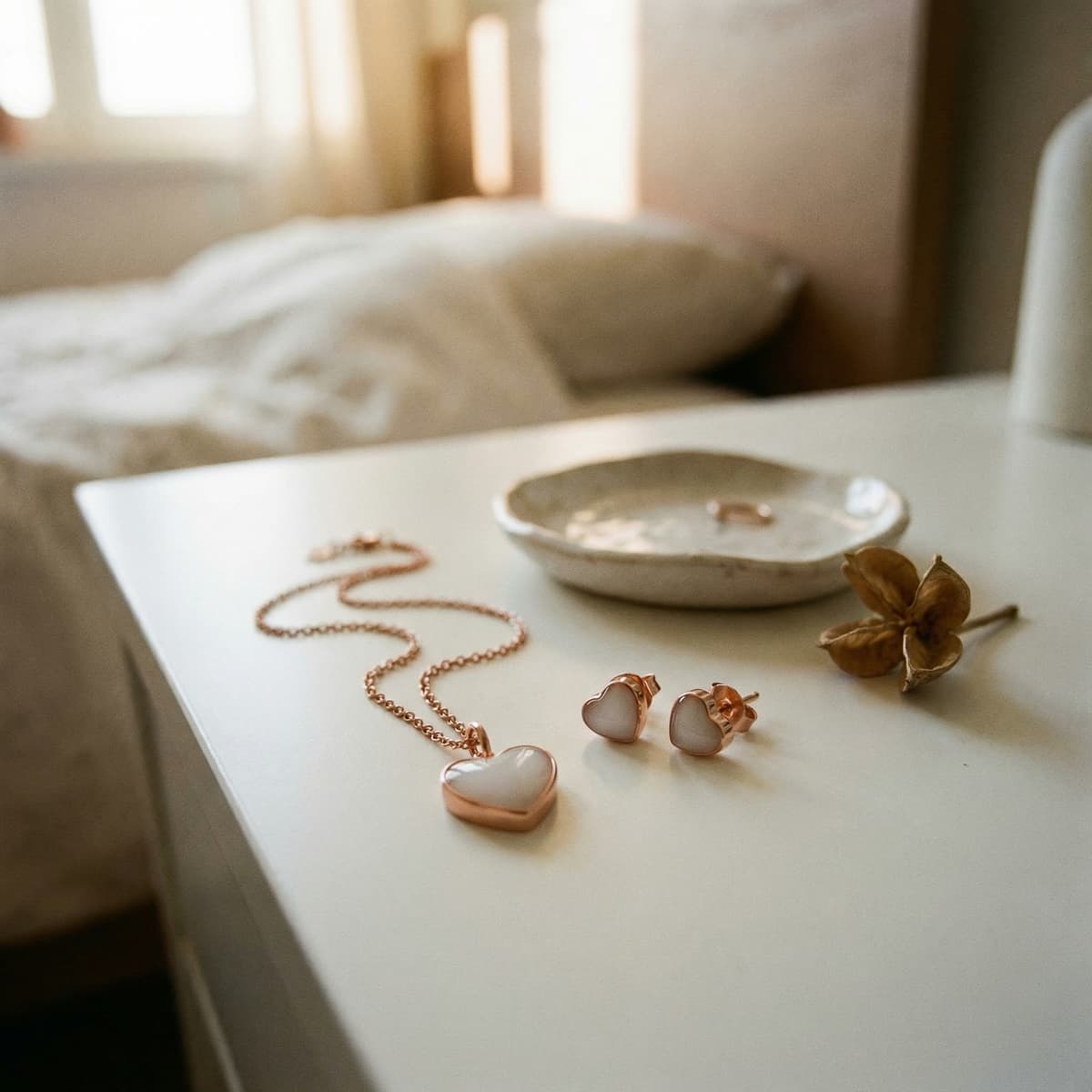 Rose-gold heart necklace and matching stud earrings with milky white resin displayed on a bedside table in soft natural light, a delicate milk keepsake jewelry set.