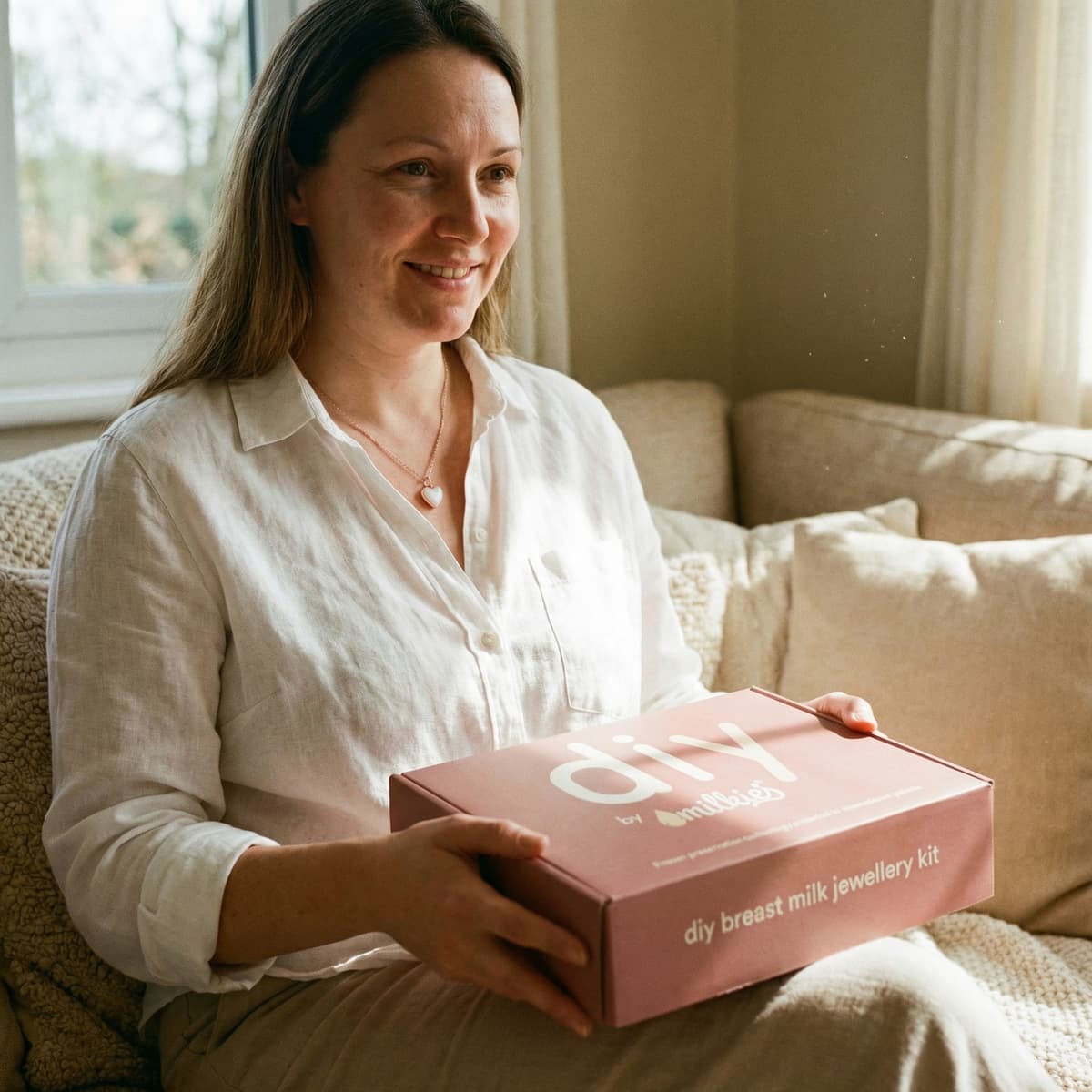 Smiling mom at home holding a DIY by MILKIES breast milk jewellery kit box, showing why an at-home DIY option is a meaningful motherhood keepsake for creating a private, hands-on memento.