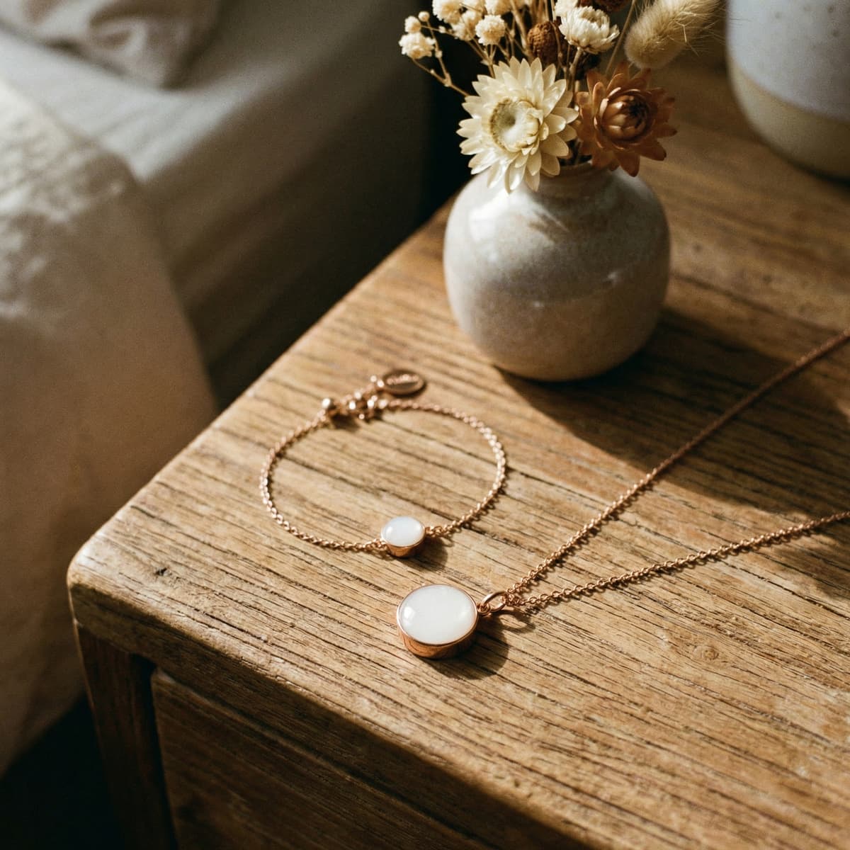 Rose gold breastmilk keepsake jewelry set with necklace and bracelet featuring milky white resin stones, styled as a thoughtful push present on a rustic wooden bedside table beside dried flowers.