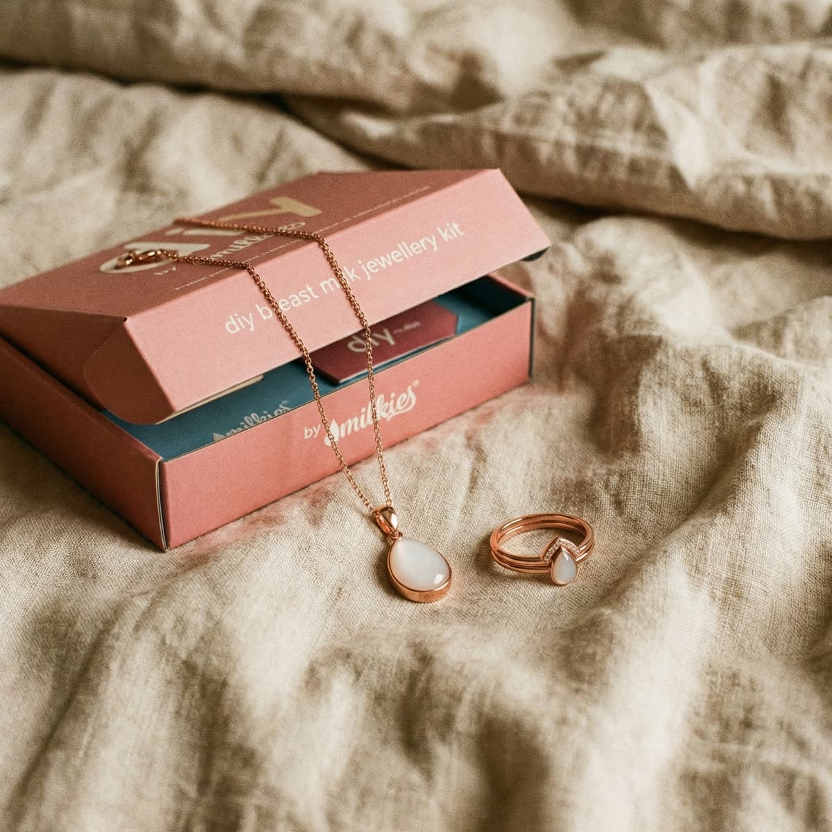DIY by MILKIES breast milk jewellery kit box on a soft bed with a rose-gold teardrop pendant necklace and matching ring, an elegant push present for wife to create a keepsake at home.