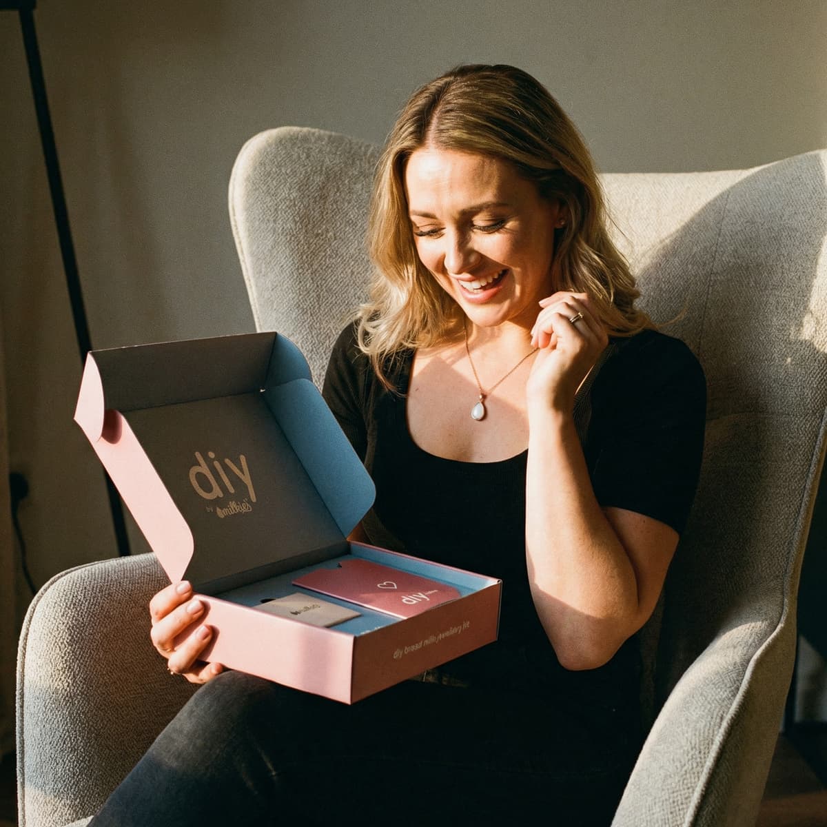 Smiling mom unboxing a DIY by MILKIES breastmilk keepsake kit at home, highlighting push present ideas with a private, easy way to create breastmilk jewelry in silver or gold-plated settings.