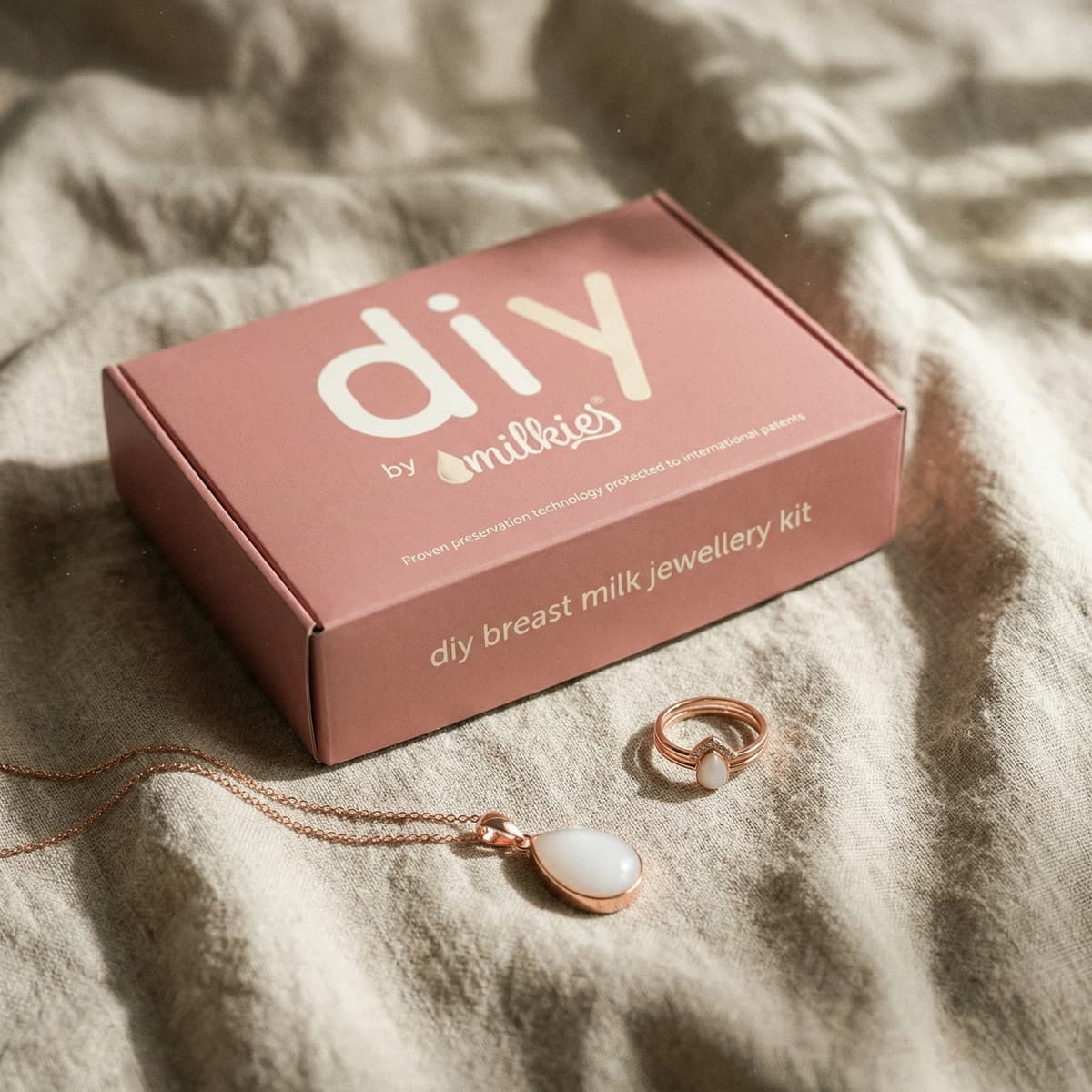Elegant push present ideas featuring the DIY by MILKIES breast milk jewellery kit box on soft fabric with a rose-gold necklace pendant and matching keepsake ring