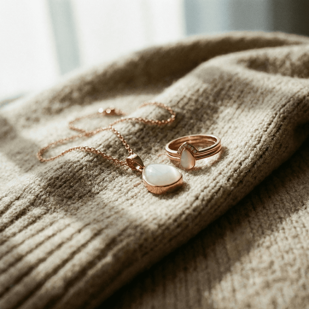 Rose gold breastmilk keepsake necklace and ring with milky white teardrop stones on a soft knit sweater, a sentimental memento for mothers stopping breastfeeding.