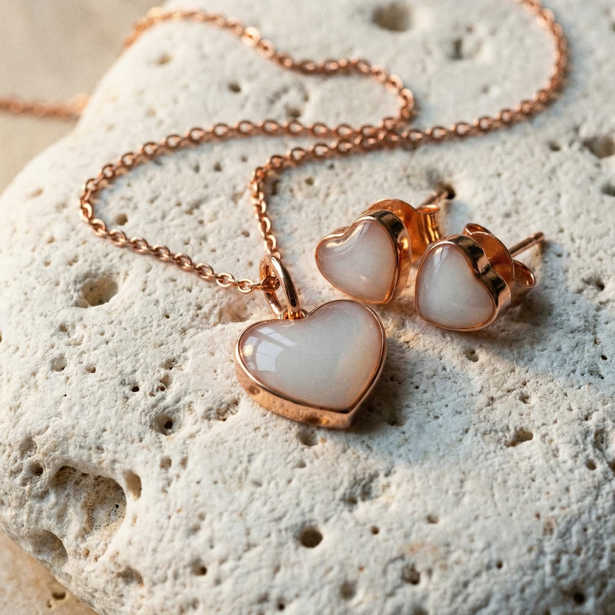 Rose gold heart pendant necklace with matching heart stud earrings featuring creamy white resin stones, a delicate jewelry set ideal as unique push presents on a textured stone background