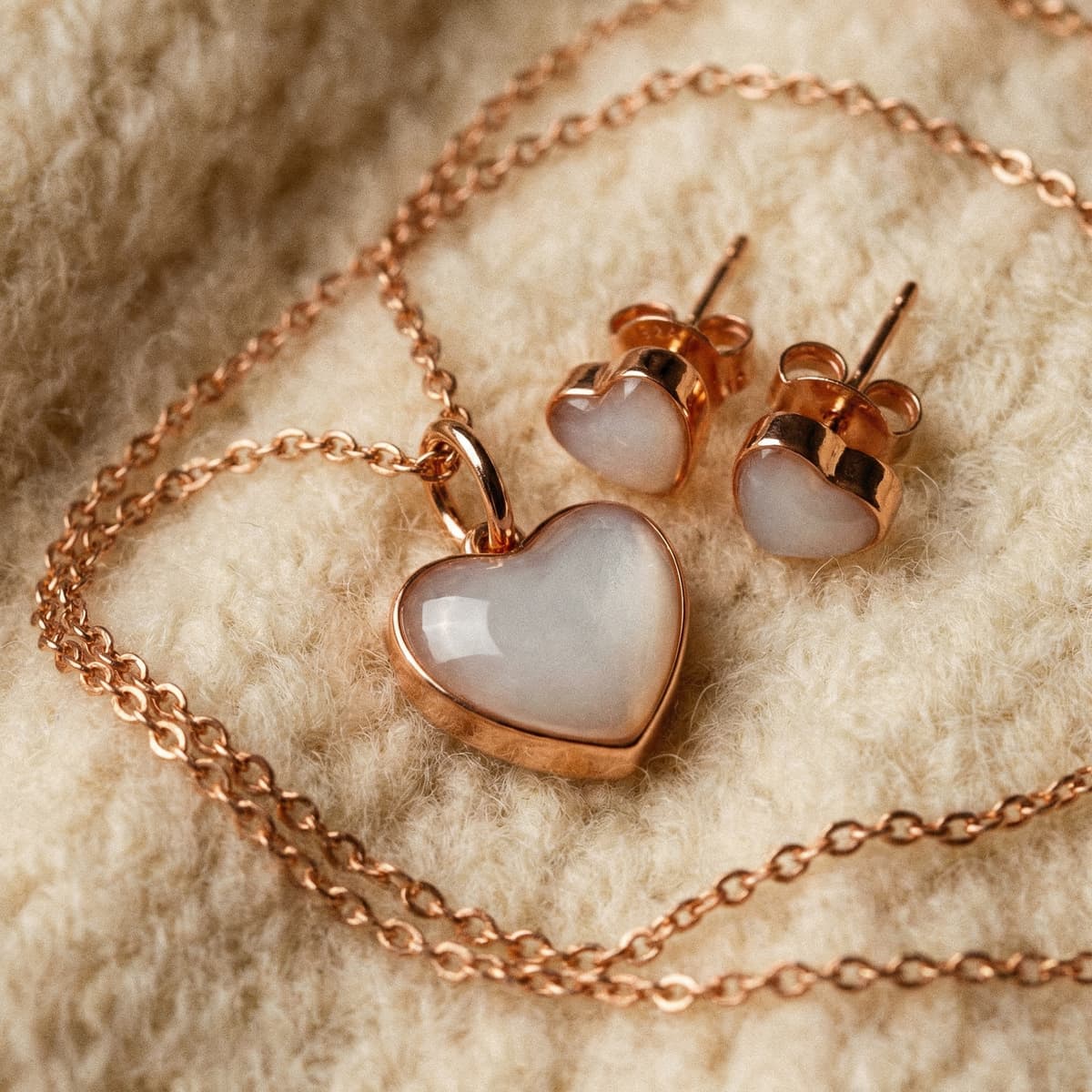 Rose gold heart pendant necklace and matching heart stud earrings with milky-white resin stones, displayed on soft cream fabric as an elegant keepsake weaning gift jewelry set.