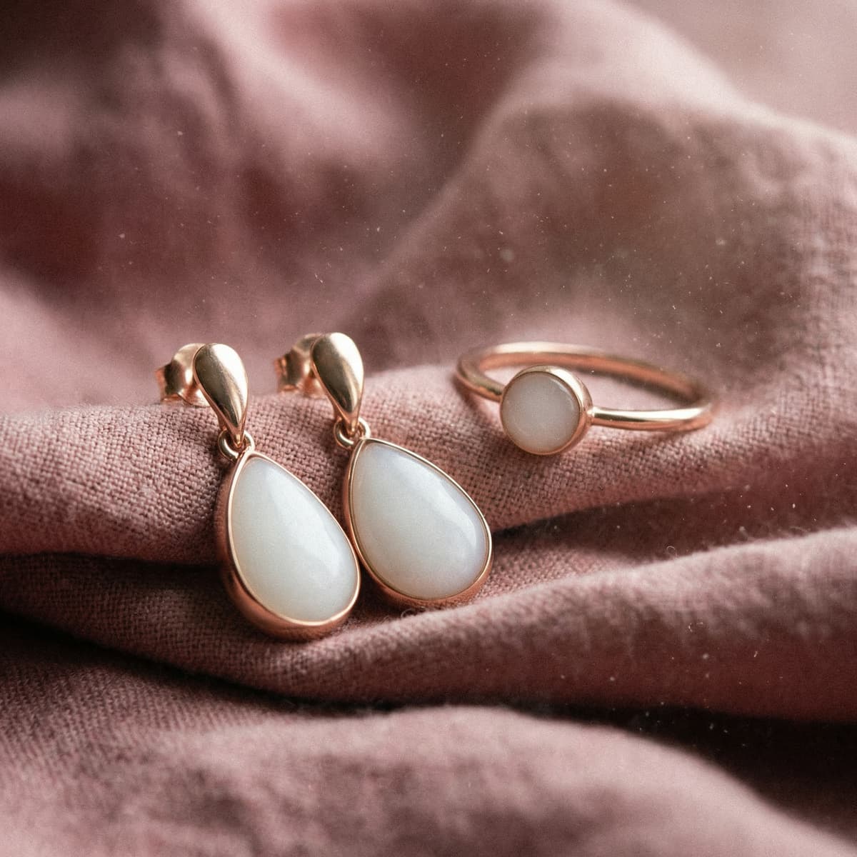 Rose-gold teardrop earrings and a matching ring with milky white resin stones on soft pink fabric, showing results made with a breast milk jewellery making kit.