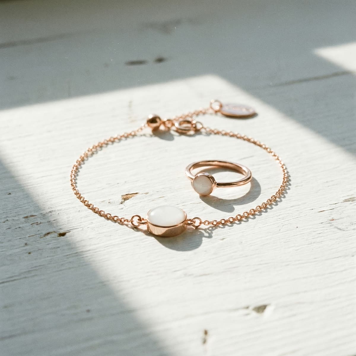 Rose gold bracelet and matching ring with milky white resin stones in soft sunlight on a white surface, showcasing a breastmilk keepsake made using a breastmilk bracelet diy kit.
