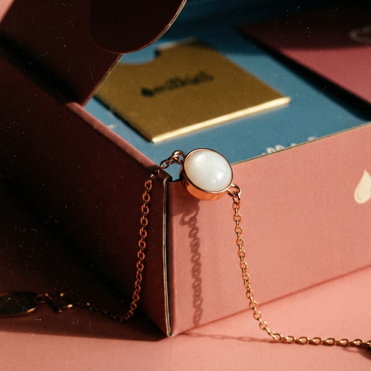 Elegant gold chain bracelet with a round milky-white resin breastmilk charm on a pink jewelry box, showcasing a breastmilk bracelets diy making kit keepsake design.