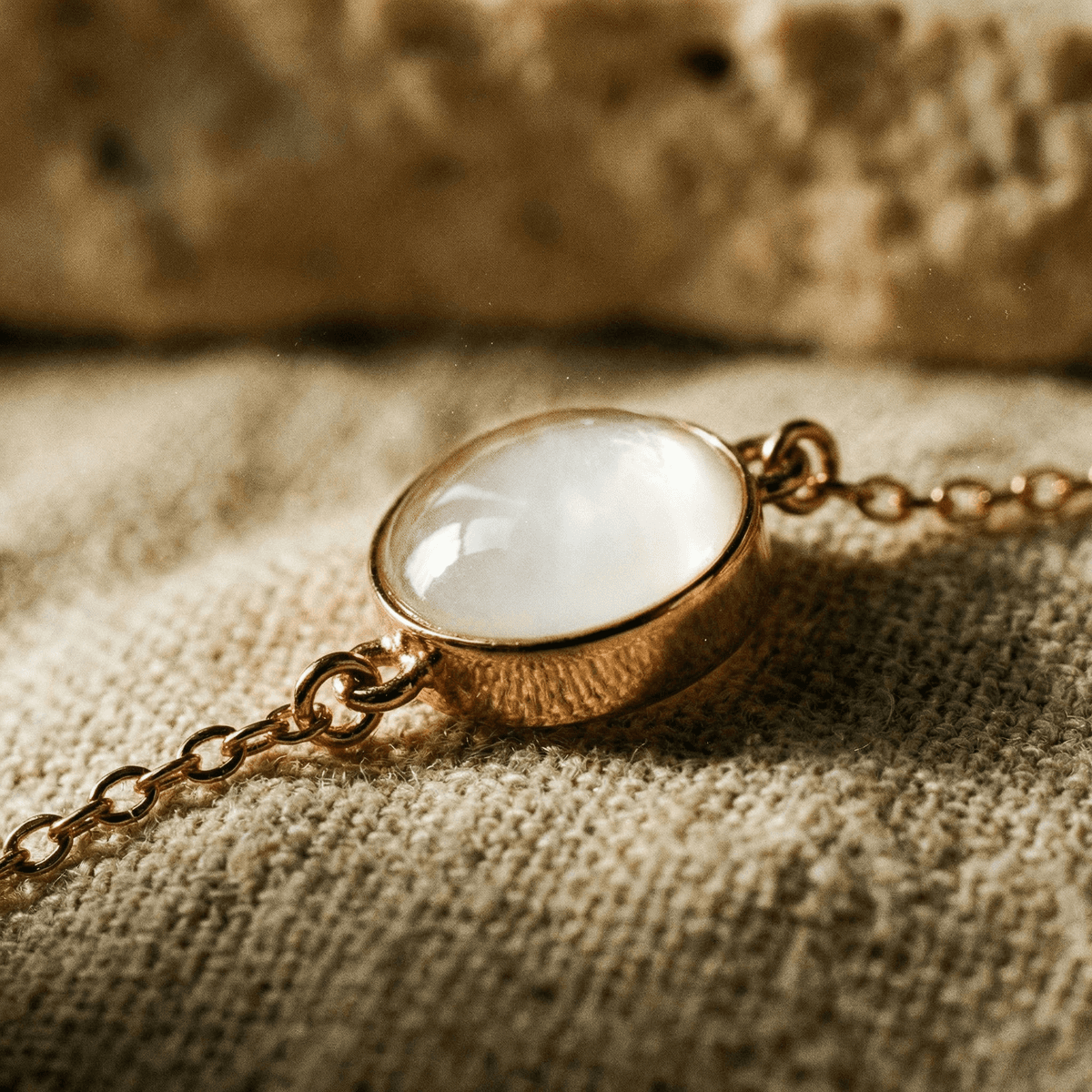 Close-up of a rose-gold bracelet with an oval white resin stone, showing the keepsake result made with a breastmilk bracelets making kit on soft neutral fabric.