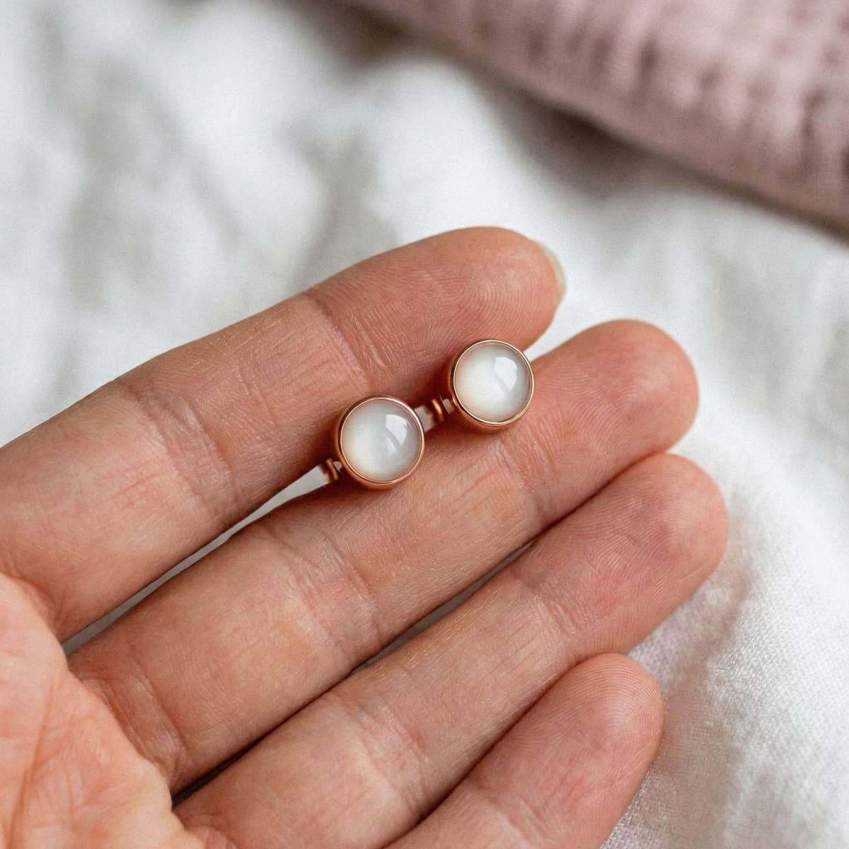 Rose gold stud earrings with milky-white resin cabochons displayed on a hand, showcasing a breastmilk earring diy making kit keepsake style in a close-up shot.