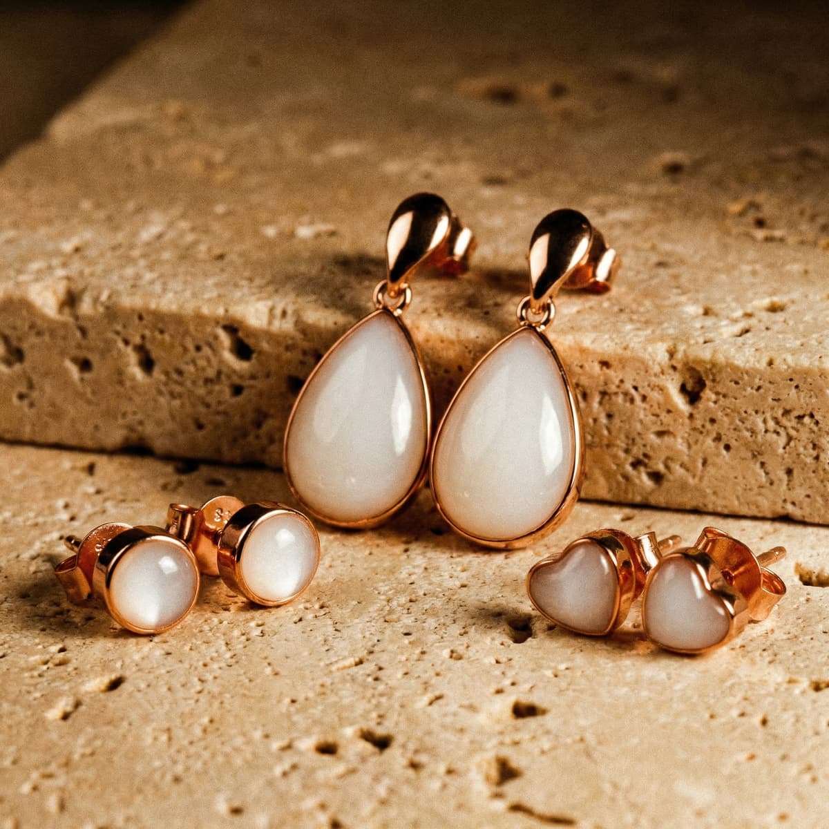 Rose gold breastmilk keepsake earrings with teardrop dangles and matching round and heart studs displayed on a textured stone surface, made with a breastmilk earring diy making kit.
