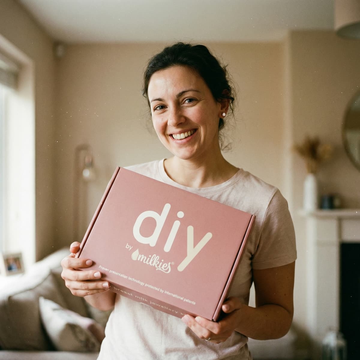 Smiling mom holds a pink DIY by MILKIES box, showing why a breastmilk earring diy making kit is a convenient at-home way to create a personal breastmilk keepsake.