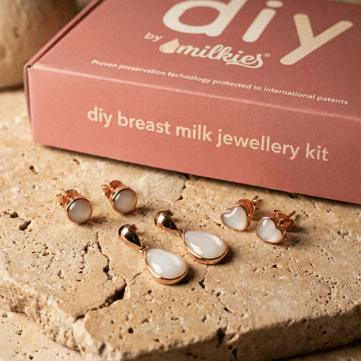 Rose-gold breastmilk resin heart and round stud earrings with matching teardrop drops displayed in front of a DIY by MILKIES box for a breastmilk earrings diy making kit
