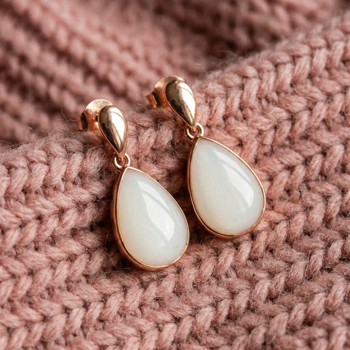 Rose gold teardrop breastmilk keepsake earrings with milky white resin stones displayed on a soft pink knit background, made using a breastmilk earrings diy making kit.