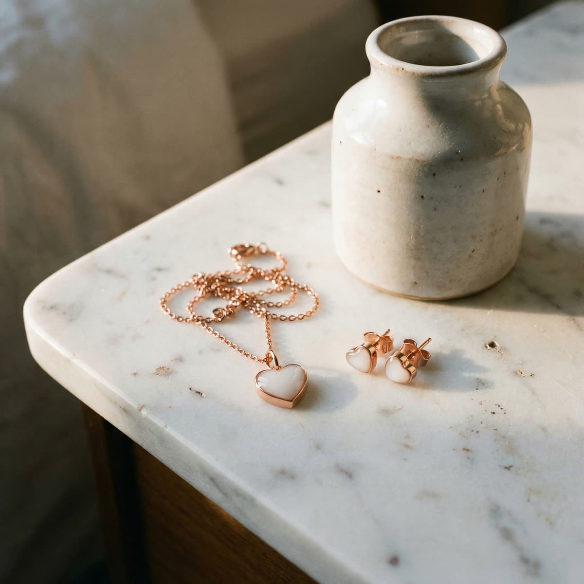 Rose gold heart pendant necklace and matching heart stud earrings styled on a marble table beside a ceramic vase, showcasing a breastmilk jewellery diy kit keepsake set.