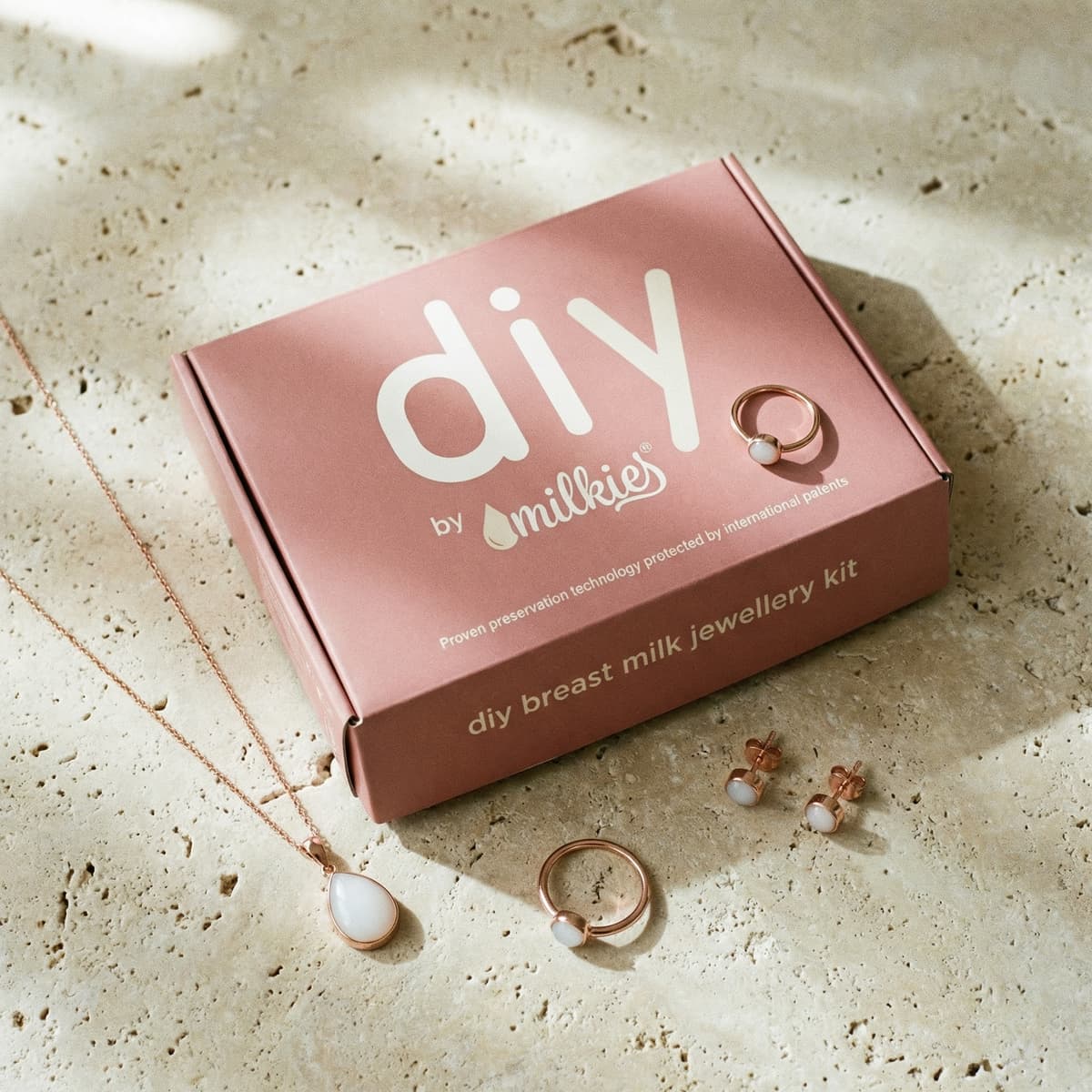 Pink “DIY by MILKIES” box featuring the patent-protected message beside a necklace, rings, and earrings from an at-home breastmilk jewelry diy resin kit for creating keepsake jewelry