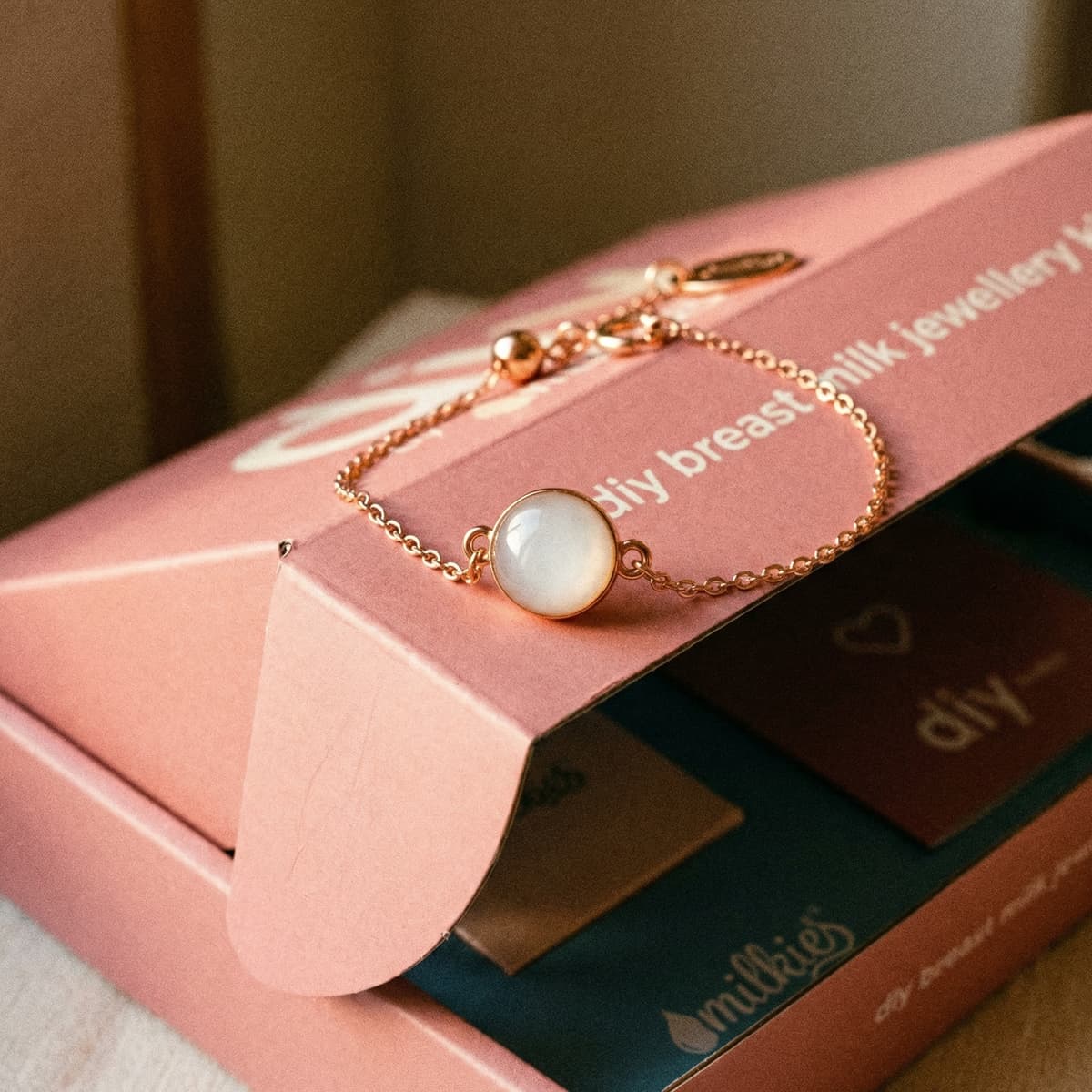 Gold chain bracelet with milky white resin charm displayed on a pink DIY by MILKIES box, highlighting a diy breastmilk bracelet making kit for creating breastmilk jewelry at home.