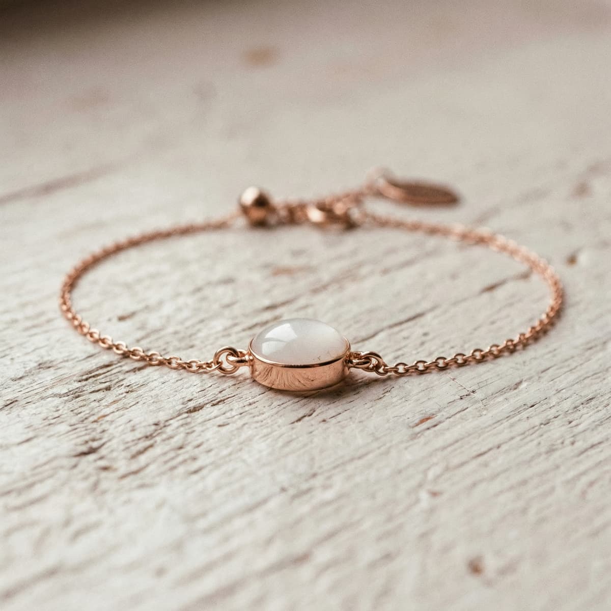 Rose gold chain bracelet featuring a milky white resin cabochon centerpiece, a finished keepsake made with a diy breastmilk bracelet making kit on a rustic white wooden surface.